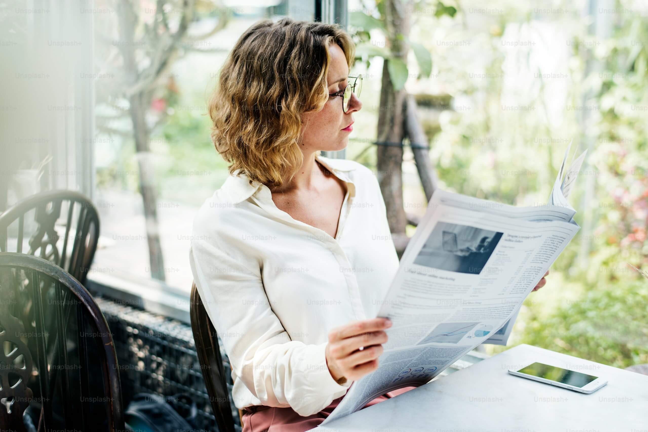 Foto de uma mulher lendo um jornal em um ambiente tranquilo