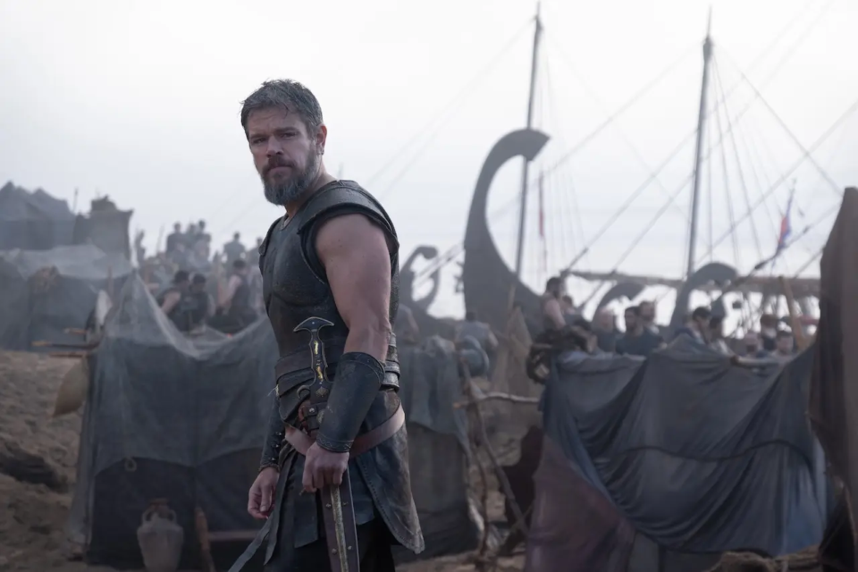 Matt Damon como Odisseu em cena de “A Odisseia”, diante de navios e tendas de um acampamento