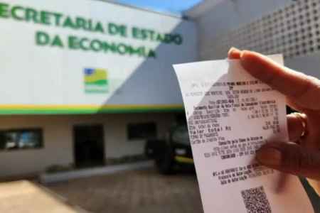 Pessoa segura nota fiscal em frente à Secretaria de Economia de Goiás
