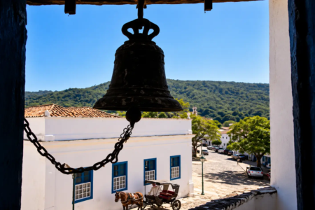 Vista de um sino histórico a partir de uma torre, com casarões coloniais, ruas de pedra e paisagem ao fundo, na cidade de Goiás. (Foto: Glauber Mattos/)